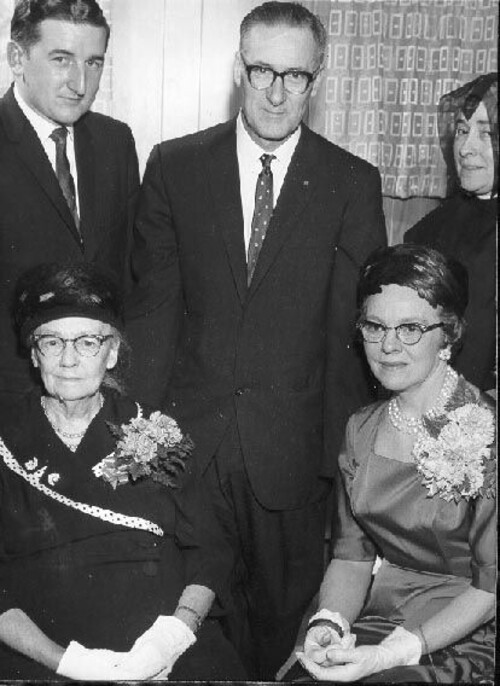 Laurier Carrière, entouré de quatre personnes en tenue élégante, dont deux femmes âgées assises.